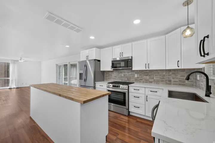 Bright kitchen featuring white shaker cabinetry, stainless steel appliances, a wood-finish island countertop, and a gray tile backsplash