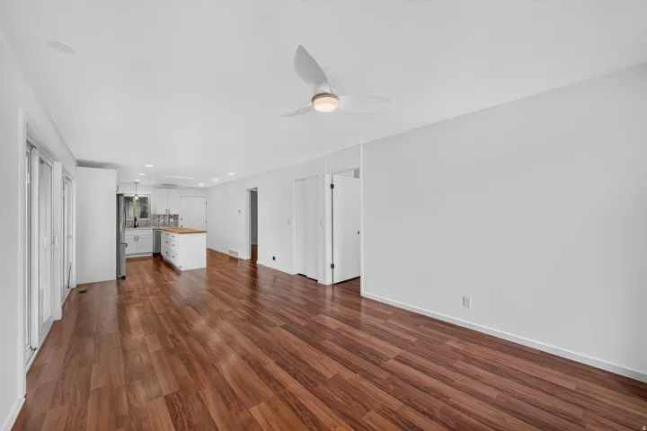 Expansive interior featuring wood-finish flooring, a contemporary ceiling fan, recessed lighting, and a kitchen with white cabinetry and a center island
