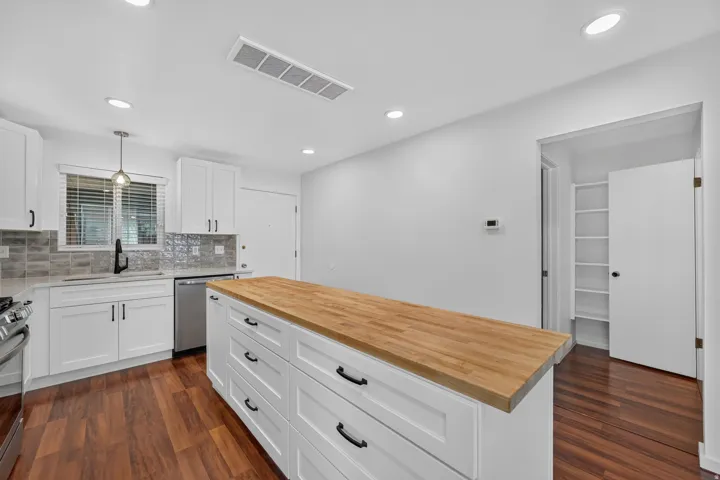 Kitchen featuring a large center island with a wood-finish countertop and white shaker-style cabinetry