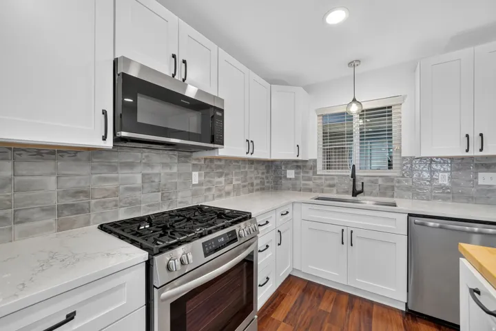 Modern kitchen featuring white shaker cabinetry, stainless steel appliances, light-toned countertops, a full height tile backsplash, and wood-finish flooring