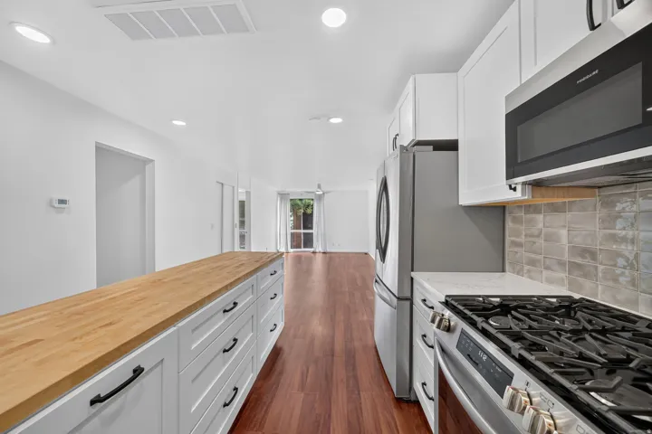 Contemporary kitchen featuring a gas range, stainless steel appliances, white cabinetry, a light-toned tile backsplash, and wood-finish flooring