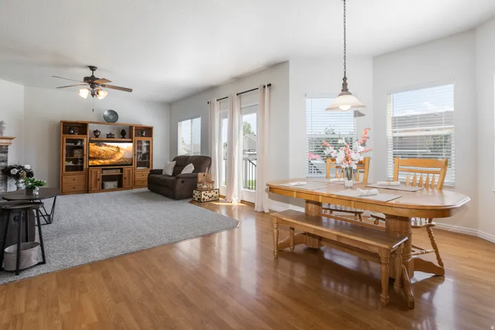 Open-concept living and dining areas featuring wood-finish flooring, a ceiling fan, and multiple large windows with blinds