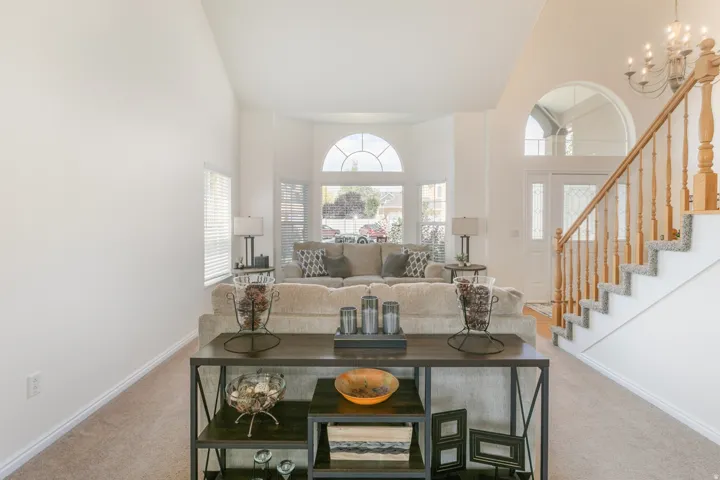 Vaulted ceilings enhance this living space, featuring a bay window with arched transom, wood flooring, and a carpeted staircase with wood banister