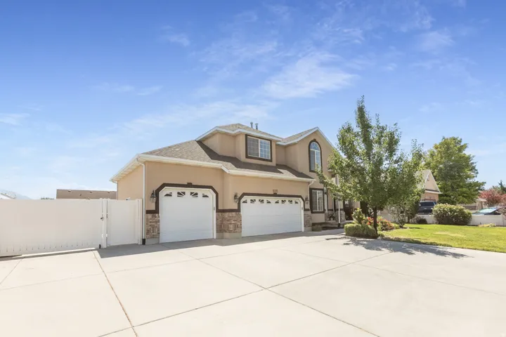 Two-story stucco exterior with stone accents, featuring a two-car garage with arched window details, a wide concrete driveway, and a white privacy fence