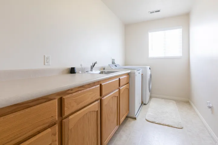 Utility room featuring wood-finish cabinetry, a neutral-toned countertop with an integrated sink, and vinyl flooring