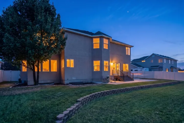 Expansive rear elevation featuring a multi-level concrete patio, a retaining wall, a mature tree, and a full privacy fence