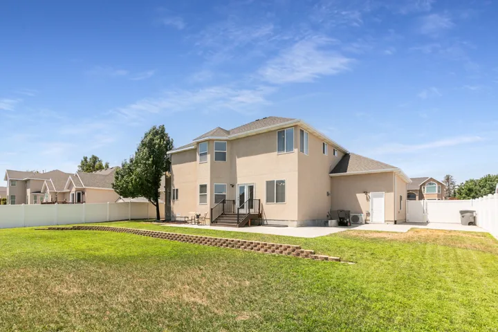 Expansive backyard with a two-story home featuring a stucco exterior, multiple windows, and a rear patio with stairs