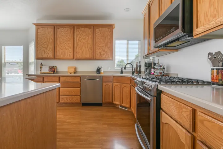 Kitchen featuring wood-finish flooring, light wood cabinetry, light-toned countertops, and stainless steel appliances including a dishwasher, range, and microwave