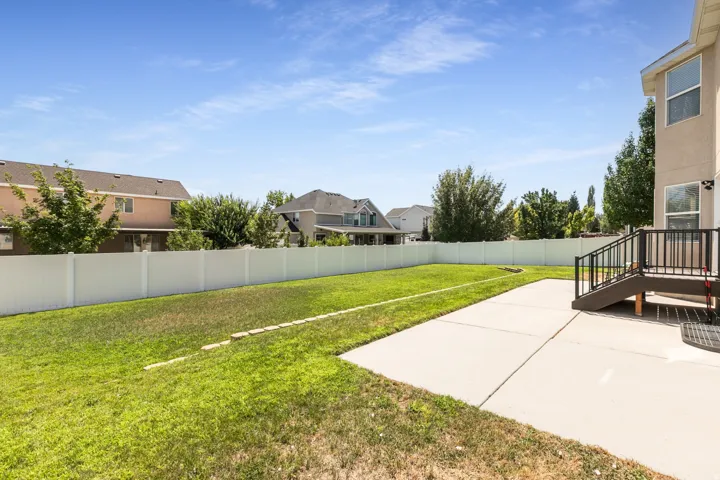 Expansive backyard featuring a manicured lawn, concrete patio, and a staircase with dark railing