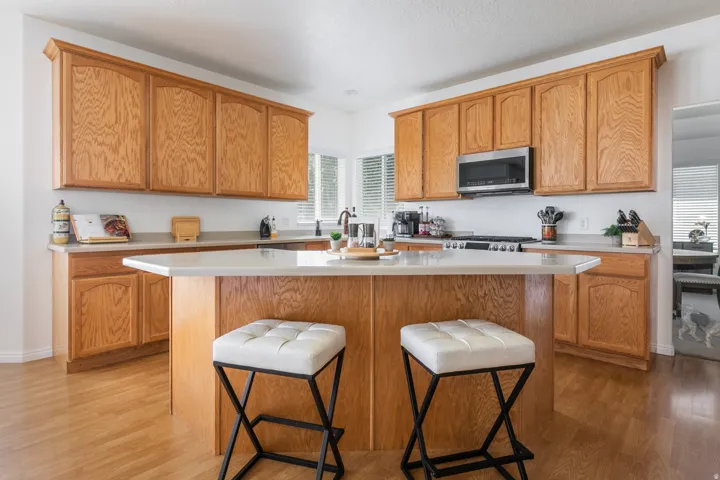 Kitchen featuring abundant light wood cabinetry, a central island with countertop seating, light-toned countertops, wood-finish flooring, and a stainless steel microwave