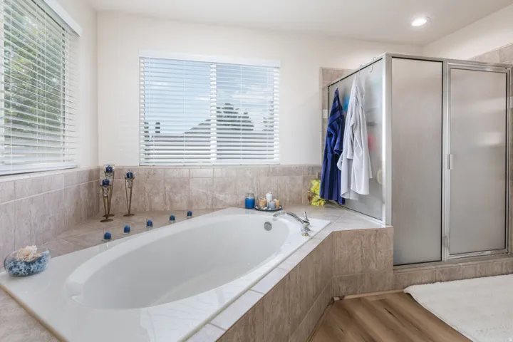 Bathroom featuring an oversized built-in soaking tub with surrounding tile, a separate shower enclosure with frosted glass, and two windows with horizontal blinds