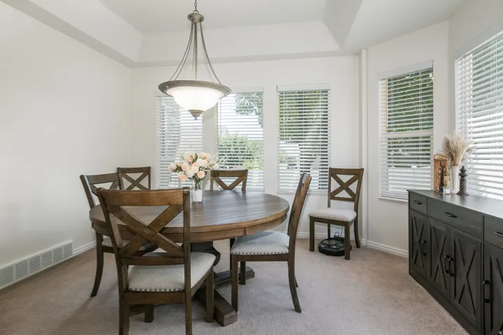 Dining area featuring a tray ceiling, multiple windows with blinds, and carpeted flooring