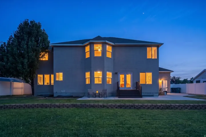 Expansive rear exterior featuring a stucco facade, multiple windows providing interior illumination, and a ground-level patio