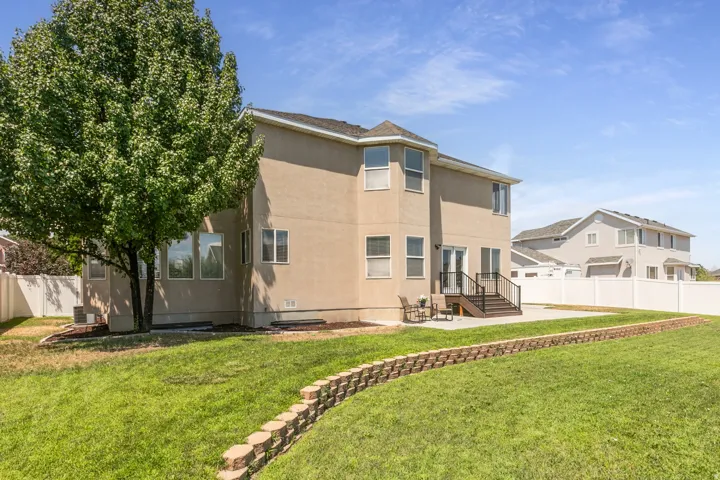 Expansive rear yard featuring a large green lawn, a multi-level block retaining wall, and a mature shade tree