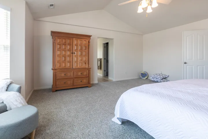Spacious room featuring vaulted ceilings, light-tone carpeting, and a ceiling fan with integrated lighting