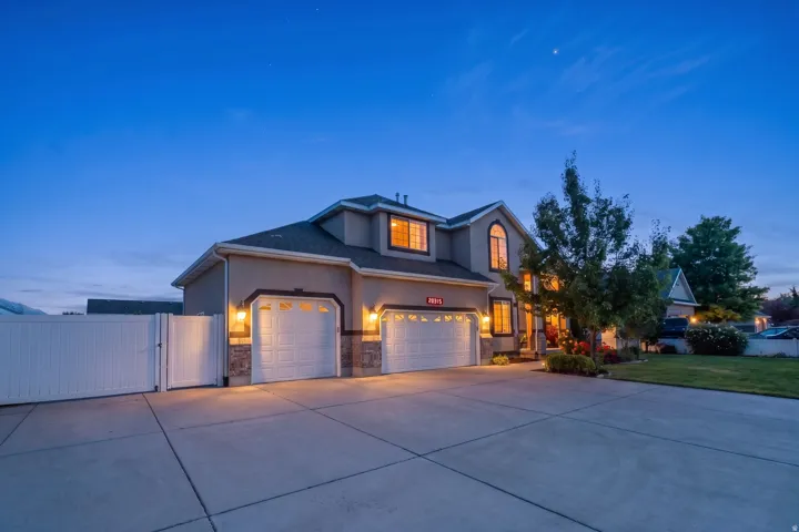 Stucco exterior featuring stone accents, a three-car garage, a concrete driveway, a white privacy fence, and mature landscaping
