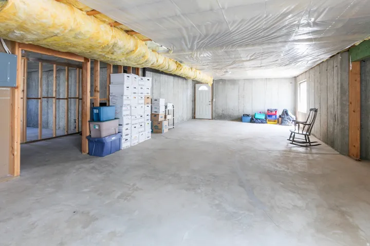 Unfinished basement with concrete flooring and exposed ceiling joists with insulation
