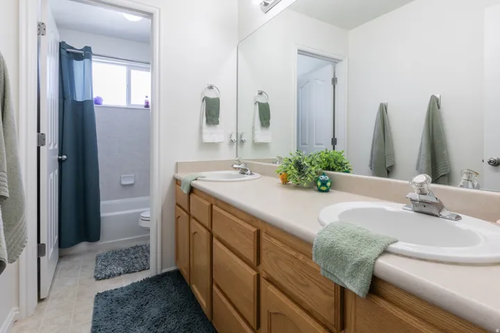 Bathroom vanity featuring dual integrated sinks with chrome faucets, a light wood-finish cabinetry base, and a full-width mirror