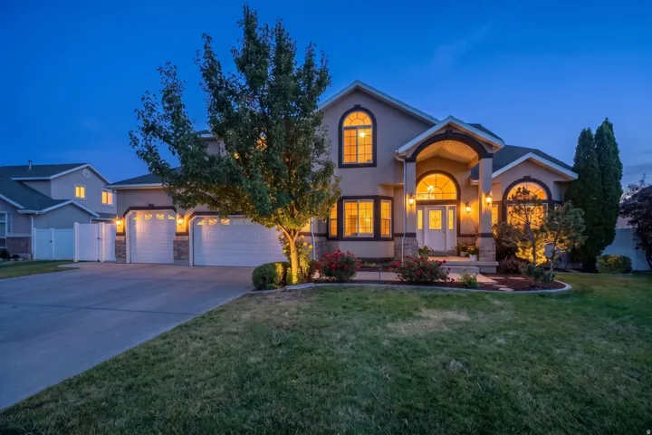 Stucco exterior residence featuring an arched portico entry with decorative columns, a multi-car driveway, and an attached three-car garage
