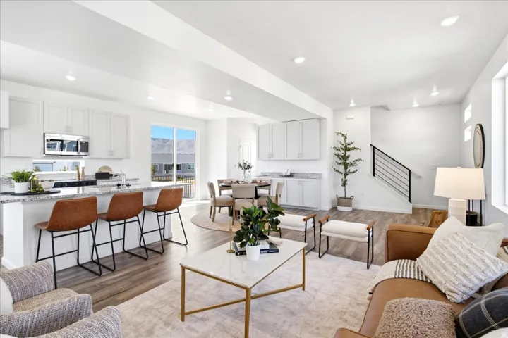 Open-concept living area featuring wood-finish flooring, recessed lighting, and a modern kitchen with white cabinetry and stainless steel appliances