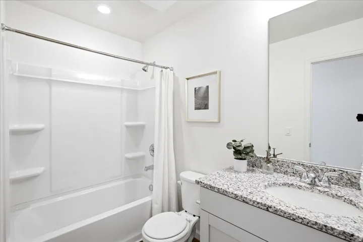 Bathroom featuring a white bathtub with a shower kit, a toilet, and a vanity with a speckled countertop