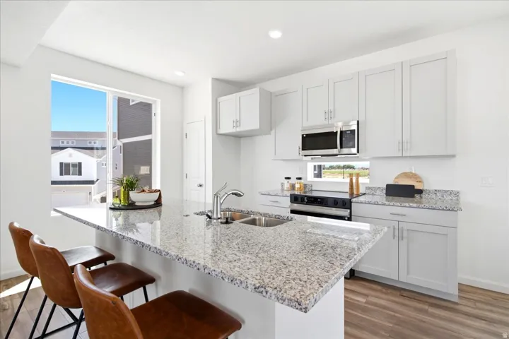 Kitchen featuring a granite island with an undermount sink, stainless steel appliances, light gray cabinetry, and wood-finish flooring