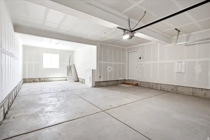 Spacious garage with concrete flooring, unfinished drywall, and a ceiling-mounted garage door opener