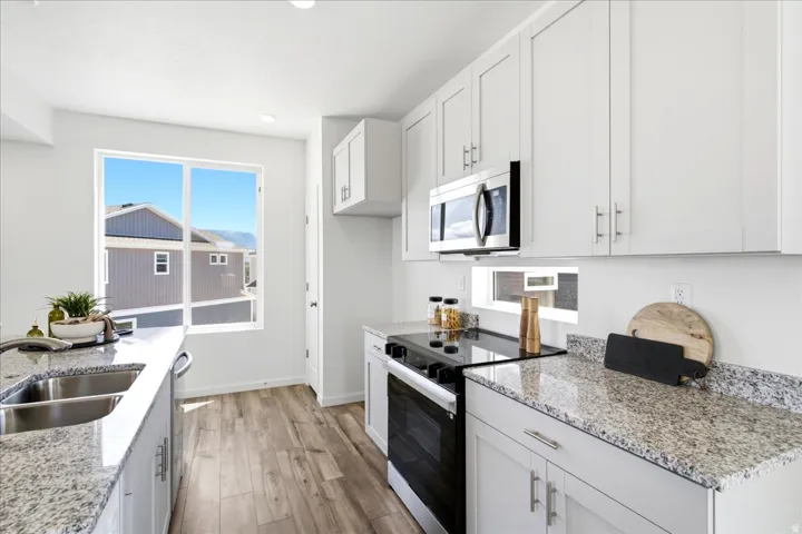 Bright kitchen featuring wood-finish flooring, white cabinetry, granite countertops, and stainless steel appliances
