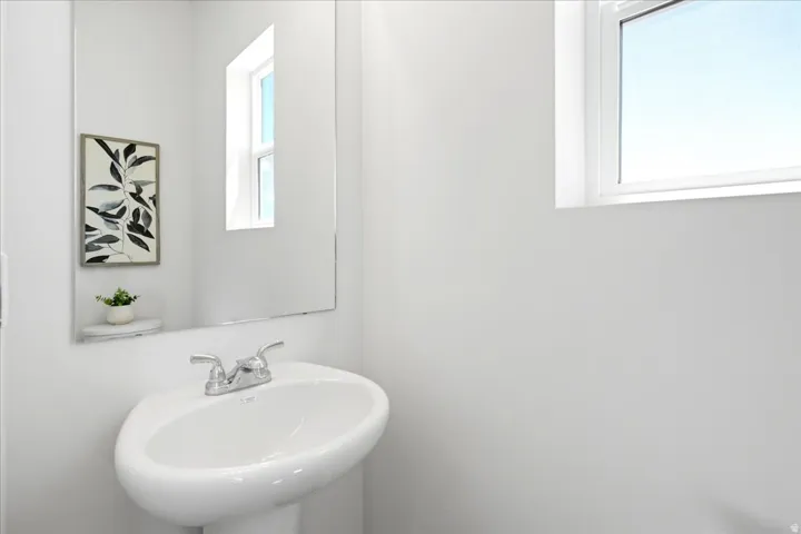 Pedestal sink with chrome faucet, large wall mirror, and a single window providing natural light