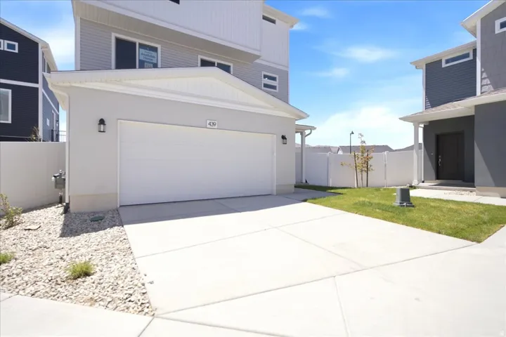 Two-story residence featuring a front-facing garage with a white door, exterior wall sconces, and a dedicated driveway