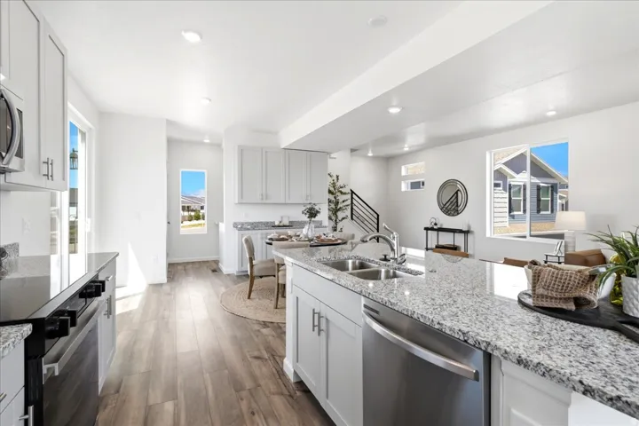 Open-concept kitchen with a large island, stainless steel appliances, wood-finish flooring, white cabinetry, and granite countertops