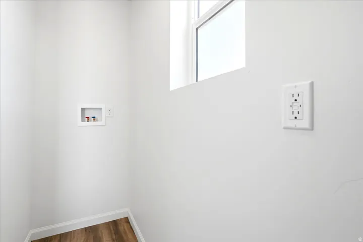 Dedicated laundry area featuring a wall box with hot and cold water hookups, a 240V outlet, and wood-finish flooring