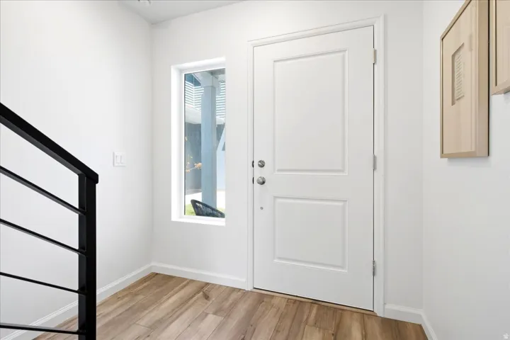 Entryway featuring wood-finish flooring, a white paneled door with polished hardware, a vertical sidelight window, and crisp white baseboards