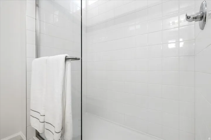 Glass-enclosed shower featuring white subway tile surround, polished chrome fixtures, and a shower pan