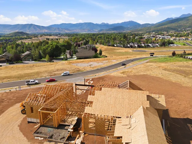 New construction property framing, multiple rooflines, asphalt paved roads, distant residential areas, and mountain scenery