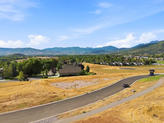 Paved road with integrated pedestrian path, surrounded by expansive natural terrain, and distant mountain scenery