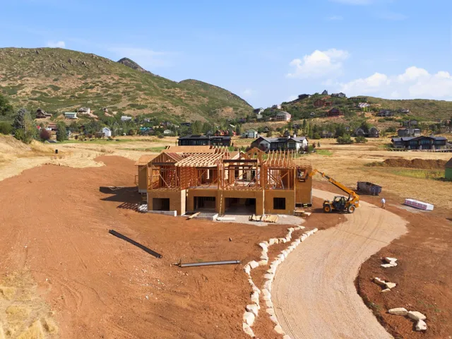 Framed residential structure with exposed lumber, graded building site, and a curved gravel driveway accented with natural stone