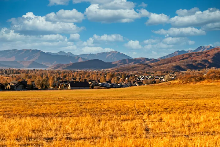Expansive open field with golden-hued grasses, complemented by distant mountain ranges and a community of homes