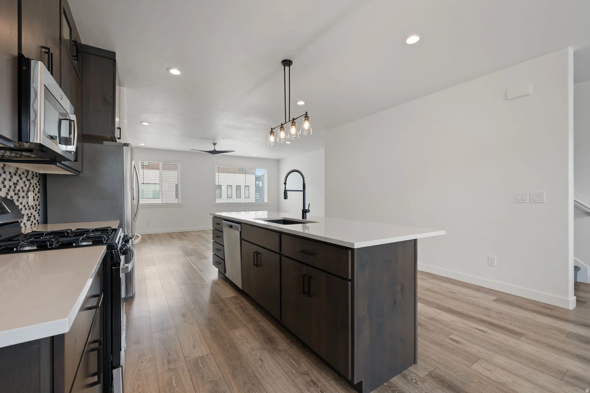 Open-concept kitchen featuring an island with a built-in sink and dishwasher, white countertops, dark wood-finish cabinetry, and stainless steel appliances