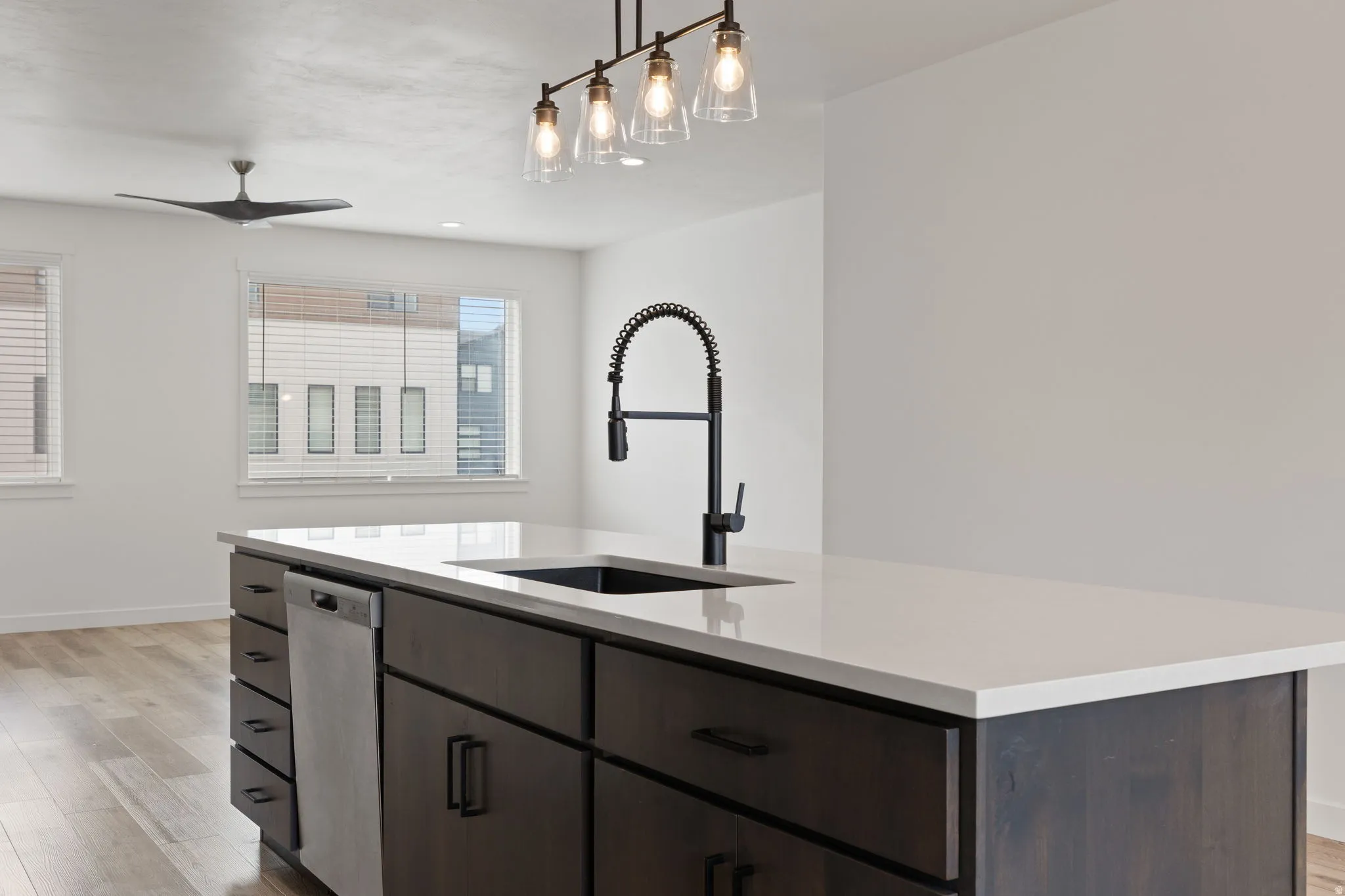 Kitchen island featuring a white countertop, dark wood-finish cabinetry, and a black gooseneck faucet with an integrated sprayer