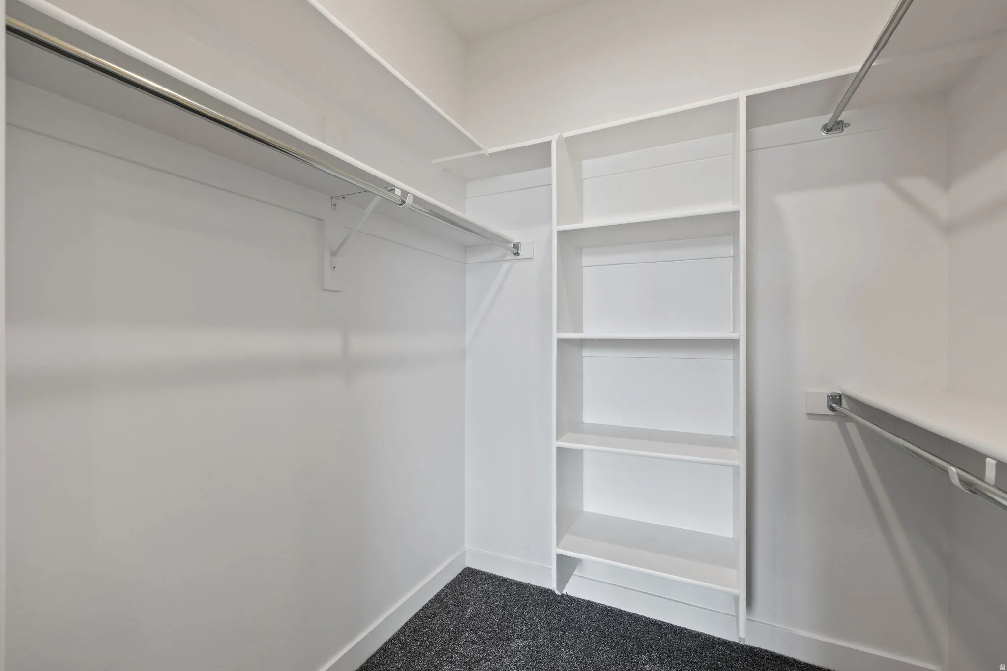 Walk-in closet featuring white walls, dark carpet flooring, and built-in white shelving