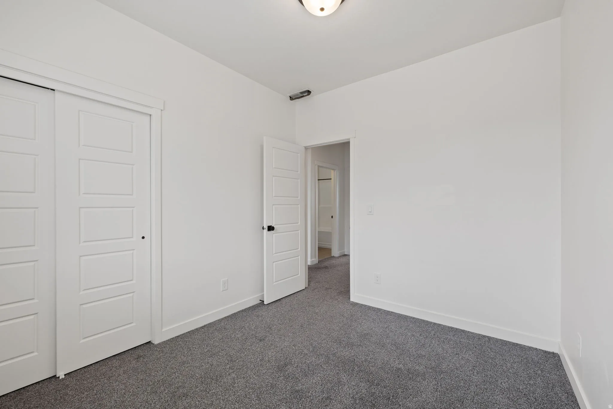 Neutral-toned room featuring a ceiling-mounted light fixture, gray carpet flooring, and white baseboards