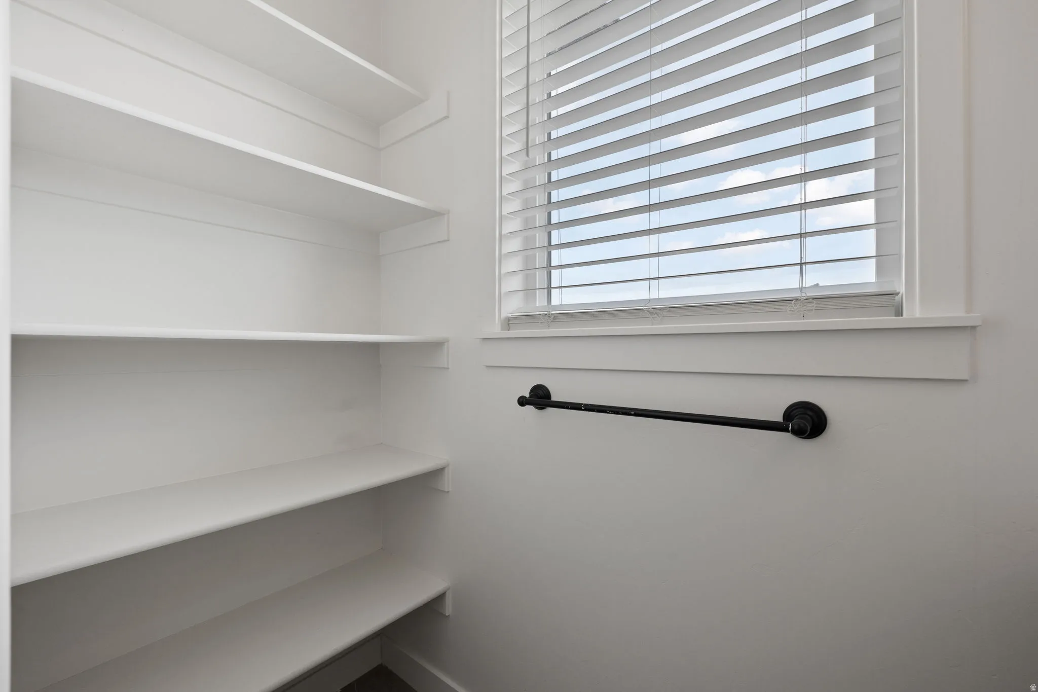 Built-in shelving with multiple storage levels, a window with horizontal blinds, and a wall-mounted black rod fixture