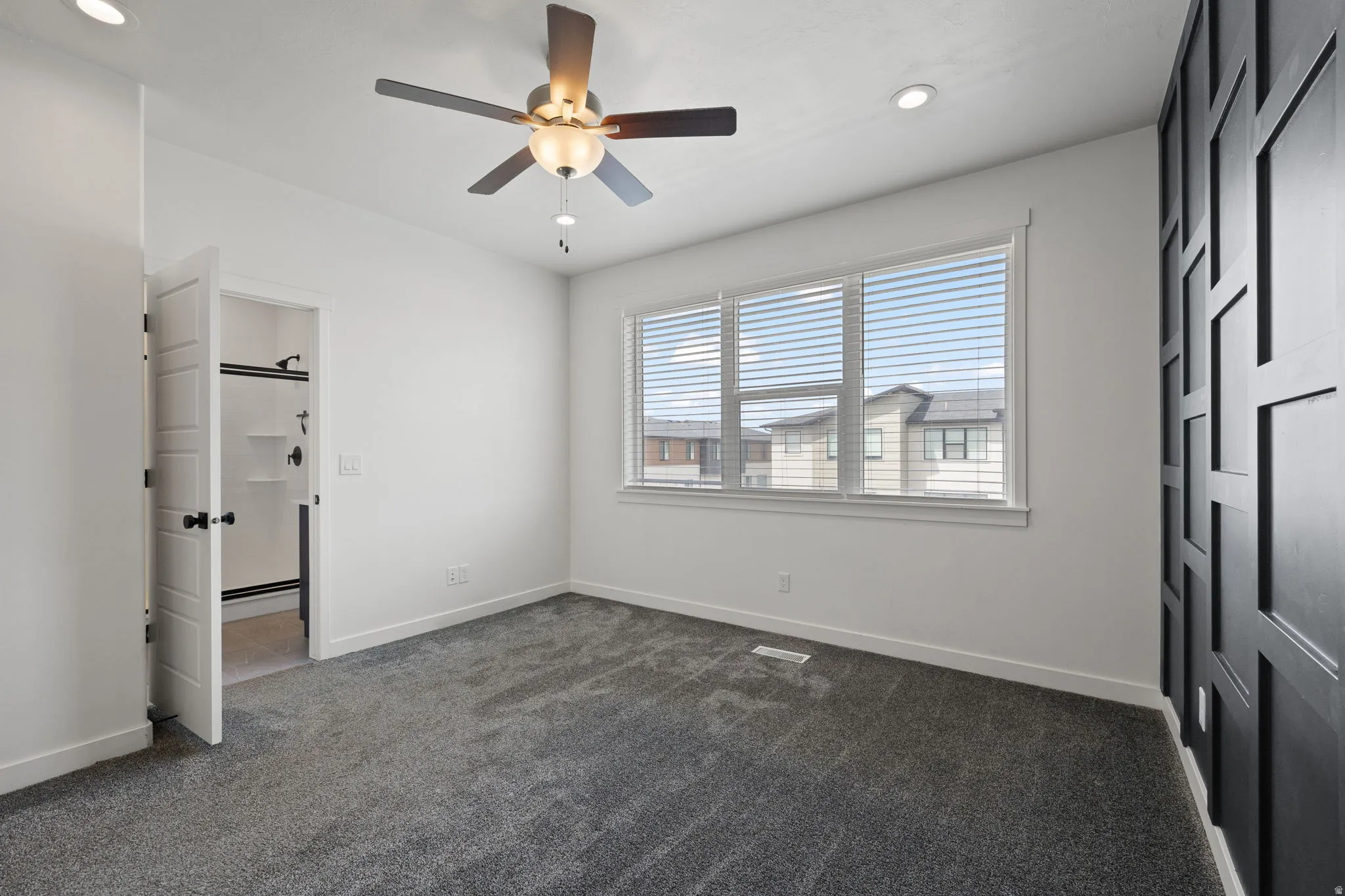 Spacious room featuring gray carpeting, a multi-pane window with blinds, and a dark accent wall with geometric paneling