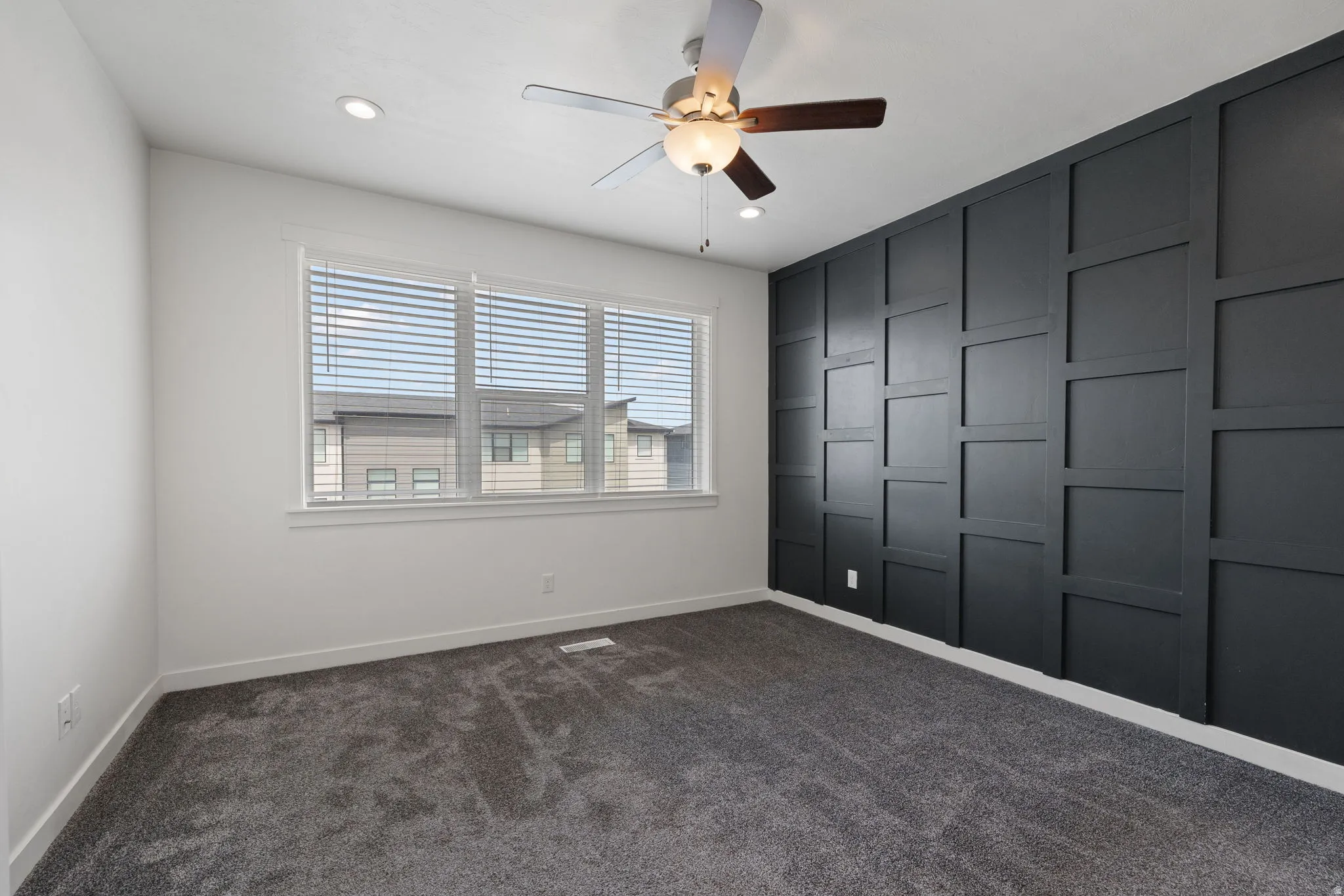 Room featuring a dark accent wall with geometric paneling, recessed lighting, and a ceiling fan