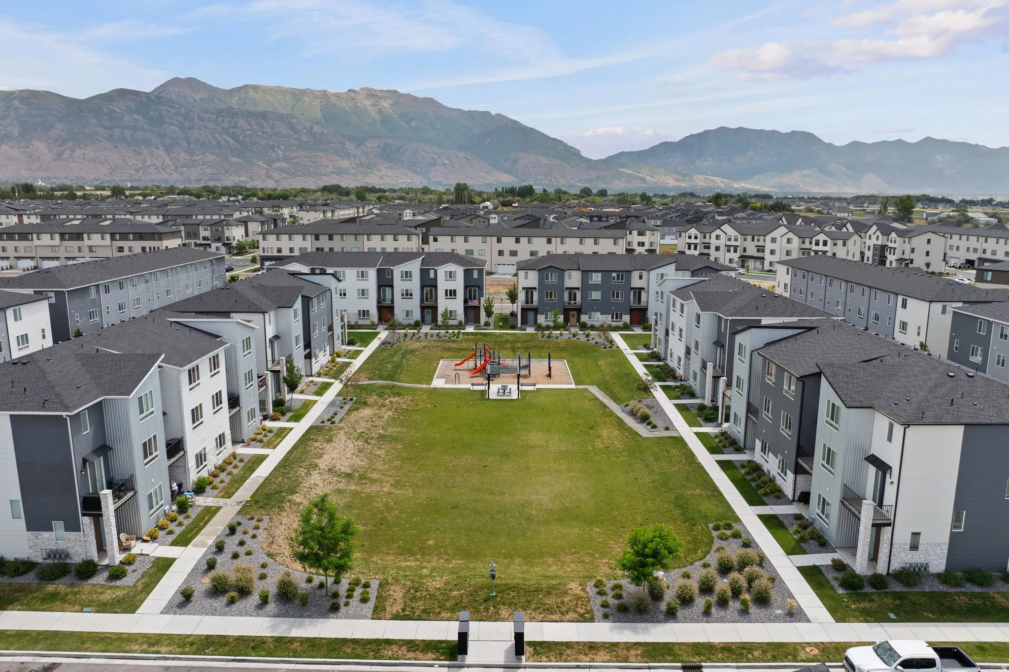 Modern townhome community featuring a central green space, children's play equipment, and mountain scenery
