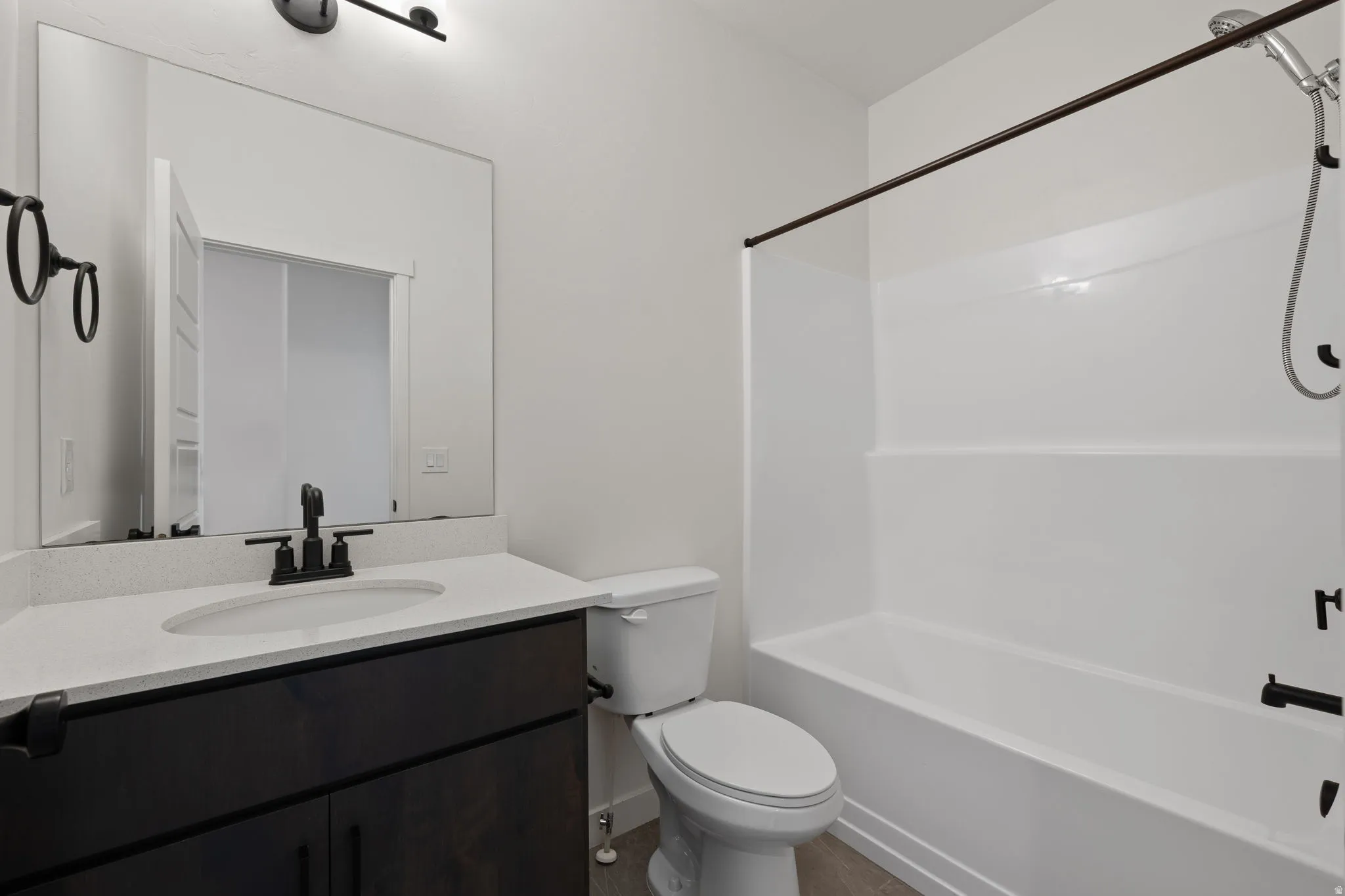 Bathroom featuring a dark wood-finish vanity with a light countertop and undermount sink, matte black faucet hardware, and a framed mirror