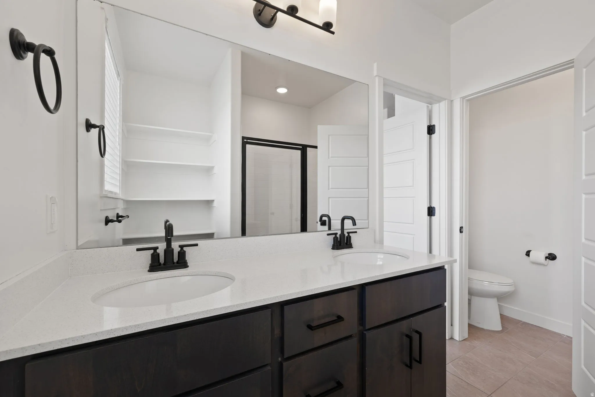 Dual undermount sinks set in a white countertop, dark wood-finish cabinetry with matte black hardware, and a large wall-mounted mirror