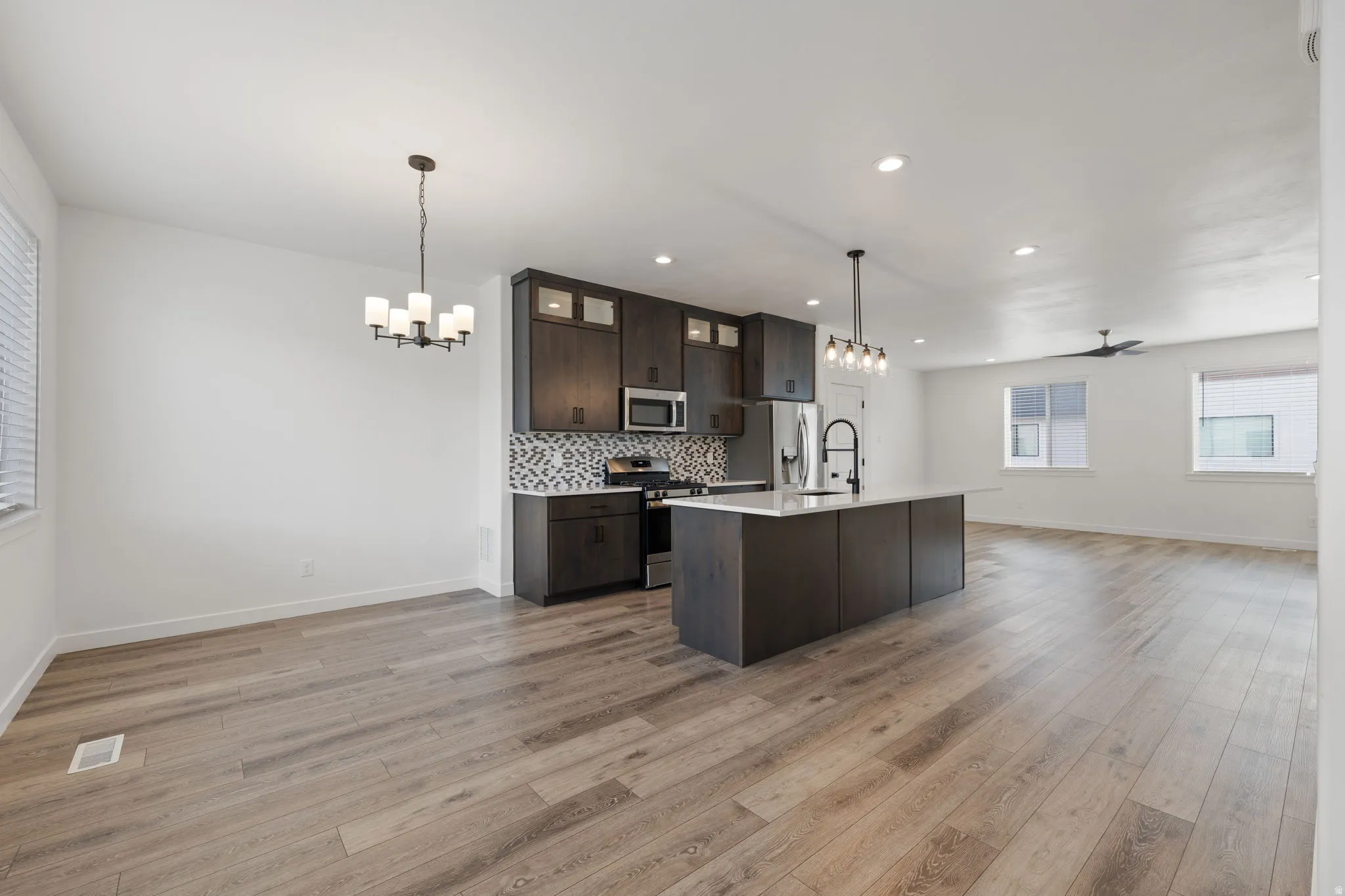 Open-concept living space featuring wood-finish flooring, a modern kitchen island with an undermount sink, dark cabinetry, and integrated stainless steel appliances