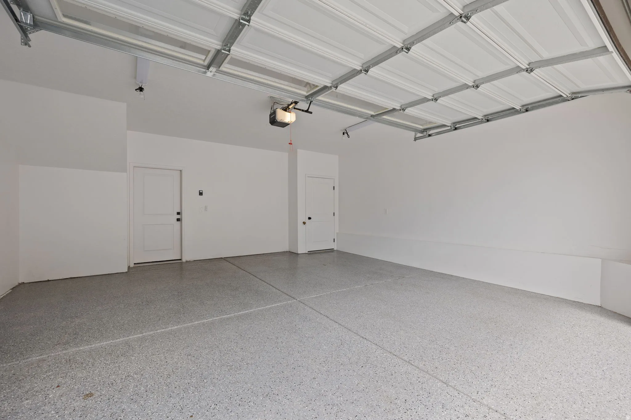 Spacious garage featuring epoxy-coated flooring, two entry doors, and an automatic garage door opener